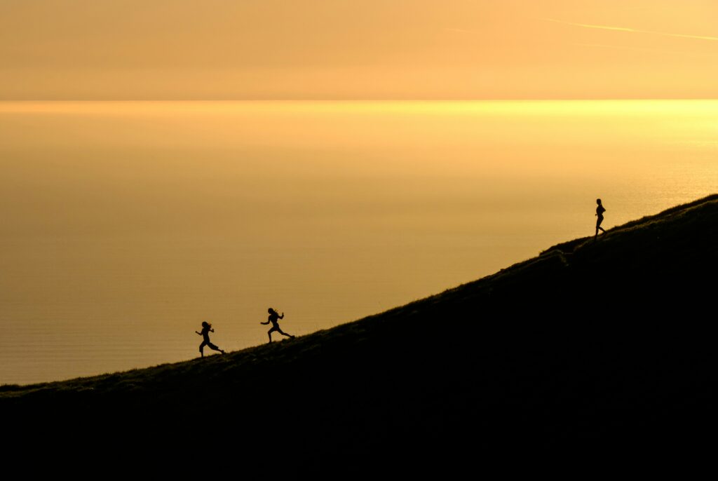 silhouettes of people running on hill at sunset